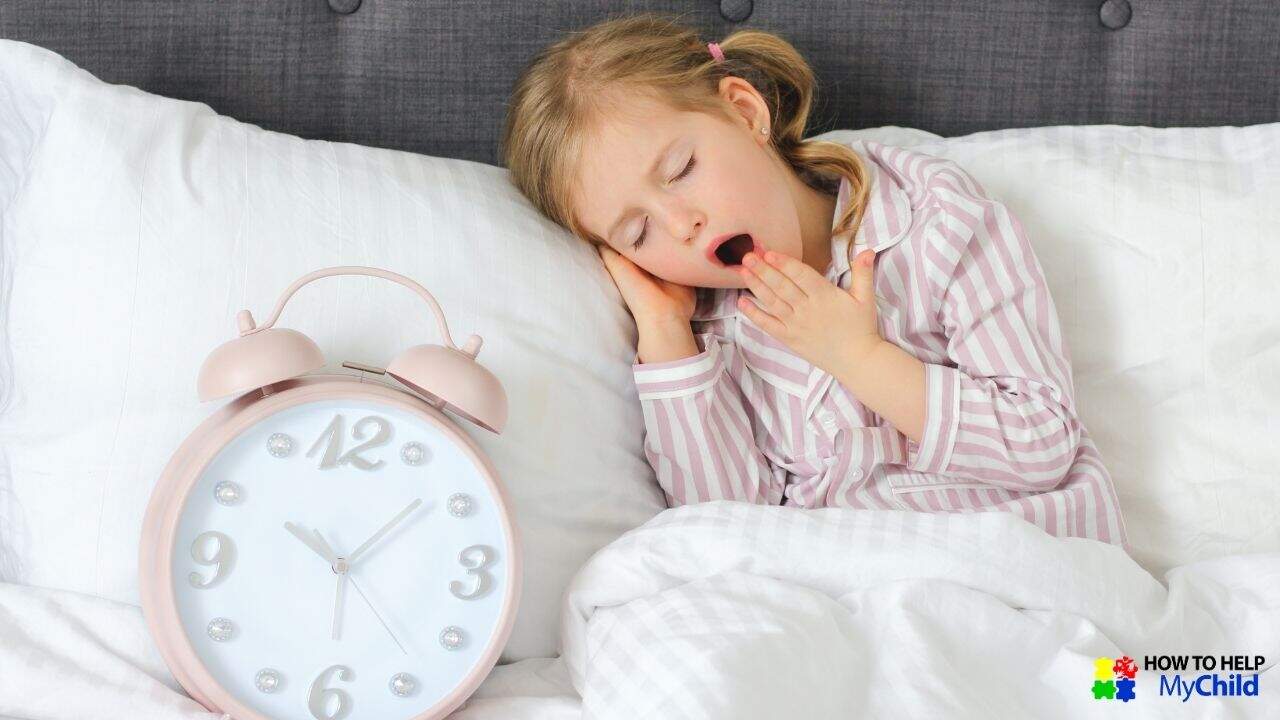 A young child in striped pink pajamas yawns while lying in bed, resting her head on her hand. A large pastel pink alarm clock sits beside her on a white pillow. This cozy bedtime scene highlights the importance of a structured bedtime routine to help children with autism and ADHD wind down for sleep. The "How to Help My Child" logo is visible in the corner.
