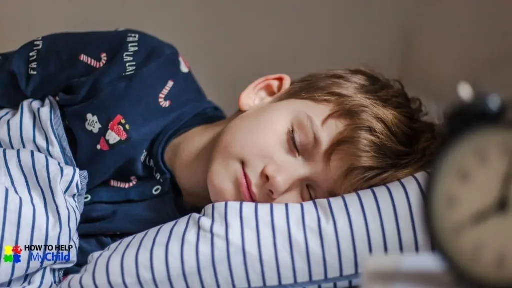 A young boy in festive navy pajamas peacefully sleeps on a striped pillow, with a blurred bedside clock in the foreground. This cozy scene highlights the benefits of a structured bedtime routine for kids with autism and ADHD, creating a calm and predictable transition to sleep. The "How to Help My Child" logo is visible in the corner.