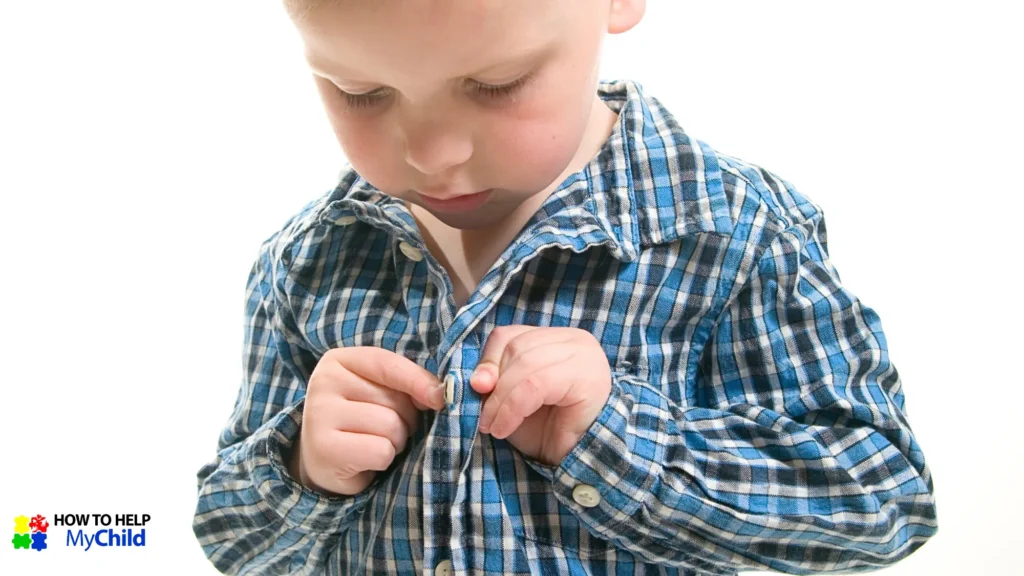Boy learning to button his shirt independently—a self-care skill that builds independence in ADHD child.