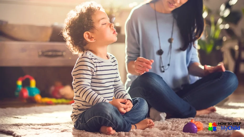 A child practices deep breathing while sitting cross-legged beside his mom. Breathing techniques are a powerful way to prevent meltdowns before they escalate.